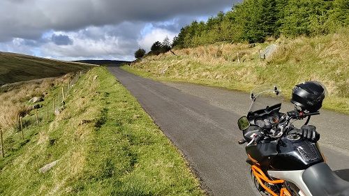 Suzuki Vstrom 650 motorcycle parked on a long road with forest on right and rolling hills on left