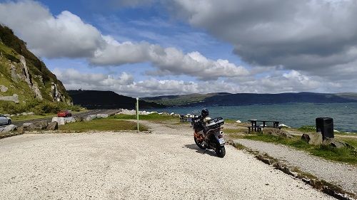 Suzuki Vstrom motorcyle parked along coast road with mountains and cloudy sky in background