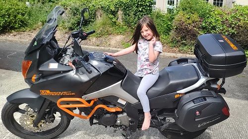 Young girl smiling and sitting on a Suzuki Vstrom 650 motorcycle