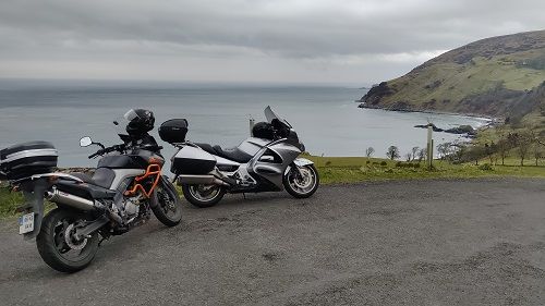 Two motorcycles parked with sea and headland in background